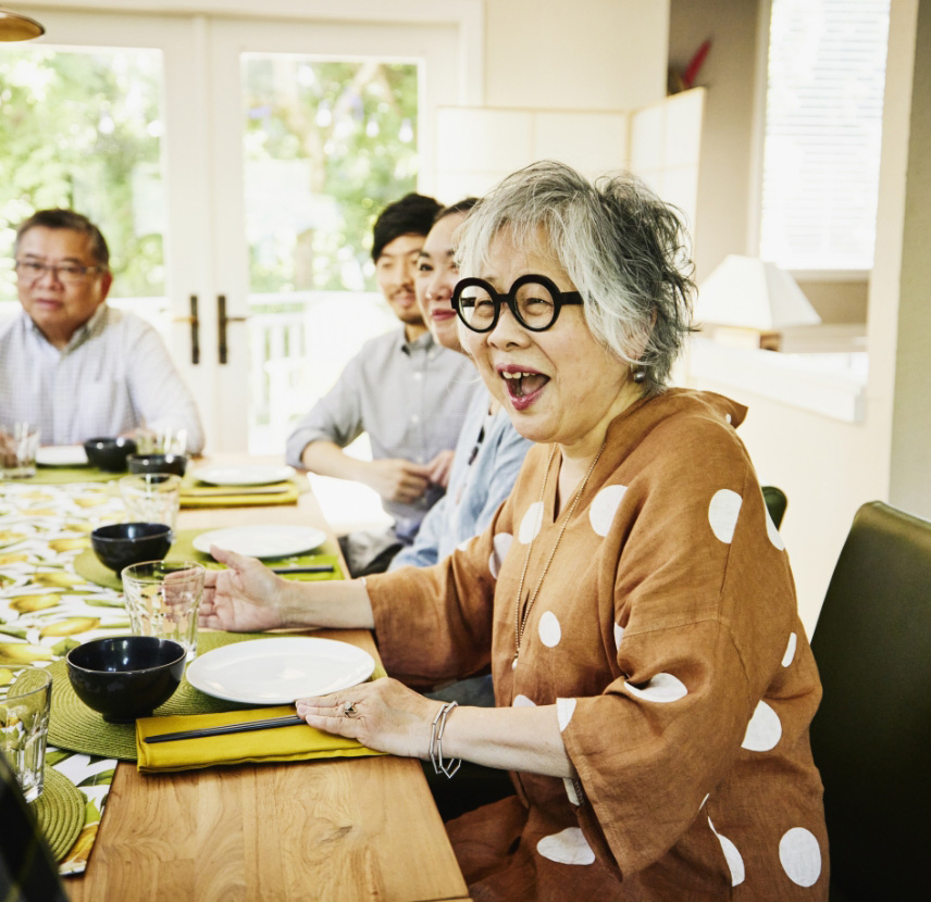 Older adult woman laughs enjoys meal with her family