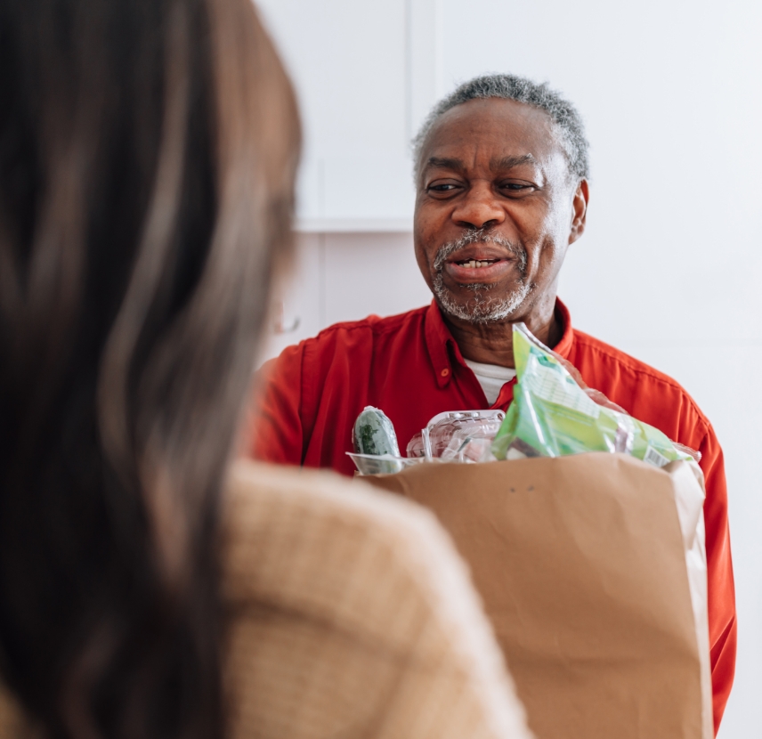 Older adult receiving bag of groceries from younger woman