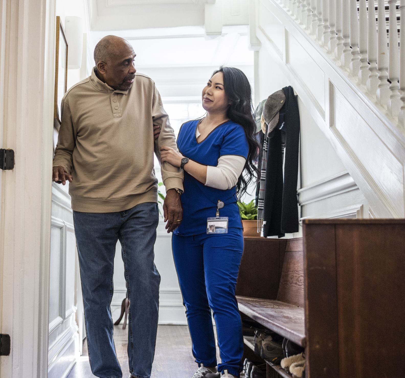 Home health aide helps older adult walk in his house.