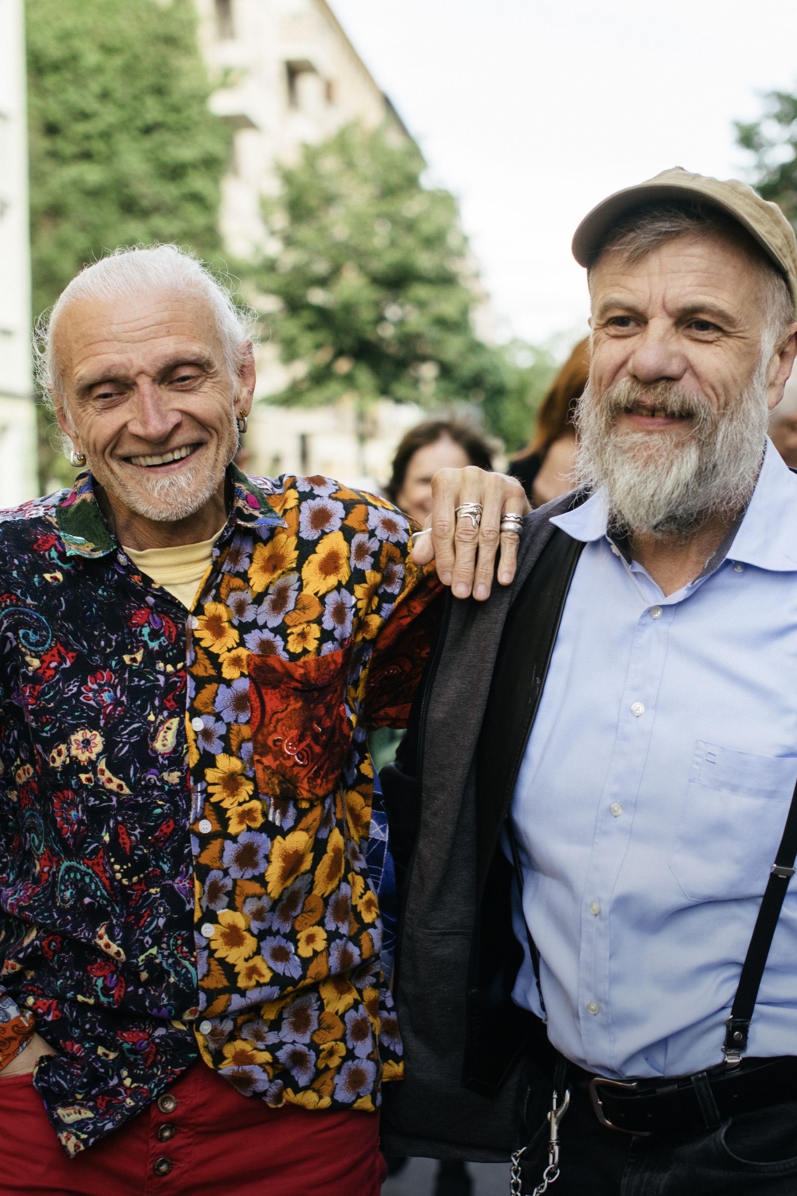 Two older adult men smiling arm in arm on a street
